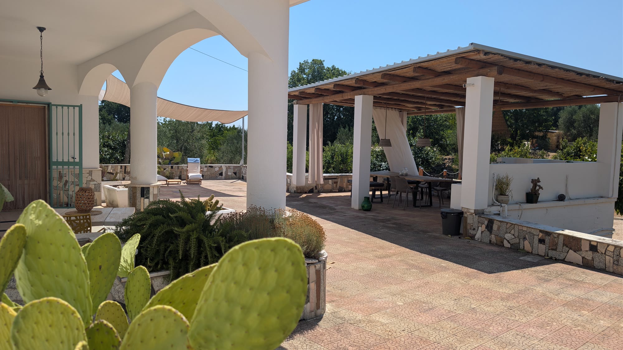 The arched loggia and, beside it, the pergola with its long table and linen curtains